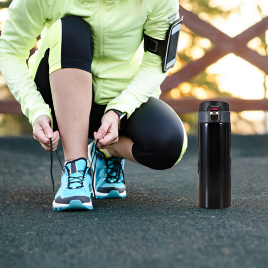 Agenouillée à l'extérieur en tenue de sport, une personne attache des baskets bleues alors qu'un Gourde métal | Flex™ de Mon Univers Sport avec un système de verrouillage innovant repose sur le sol à proximité.